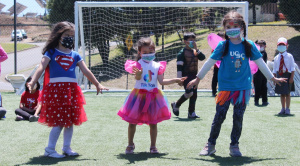 Desde el 5 de enero que la cancha del Campus San Andrés se llena de niños y niñas entre los 3 y los 13 años. Son cerca de 140 hijos e hijas de trabajadores de la UCSC, que de lunes a viernes, entre las 9 y las 13 horas, disfrutan de Verano Recreativo 2022 con juegos, música, baile y talleres de ciencias, cocina, teatro y expresión junto a un grupo de monitores, los que en su mayoría son alumnos de 2do año en adelante en las facultades de Medicina y Educación de la misma Universidad y con experiencia previa en el trabajo con menores. Carolina Baier, jefa de la Unidad de Bienestar y Formación de Personas, cuenta que este programa se lleva realizando hace 11 años y que comenzó como una actividad más recreativa durante el período de vacaciones y que con el tiempo se fueron sumando otros actores de la propia casa de estudios, convirtiéndose en “un programa más integral, no solo de recreación, sino de aprendizaje, deportivo, de vida saludable. Como Unidad y como Dirección, hemos crecido con esta actividad porque al principio participan 40 niños y ahora es con inscripción y desde diciembre nos preguntan cuándo comienza. Algunos que partieron de chiquititos, ya son apoyo de monitores o monitores fijos que enseñan a los nuevos integrantes.” Pese a la experiencia alcanzada en más de una década, realizar esta versión implicó un reto no menor. “Por la pandemia, el año pasado fue a través de modalidad sincrónica. Este año pensamos hacerlo dos veces a la semana, pero después las autoridades nos aprobaron todos los días”. Sobre los cuidados que han tenido, Carolina dice que se han regido por los protocolos Covid es decir uso de mascarilla, la cual se cambia varias veces por jornada, desinfección de manos con alcohol gel, colaciones individuales para los niños, sumado a otras acciones como la toma de PCR a los monitores una vez a la semana o informar de contactos estrechos para tomar rápidamente los exámenes, en resumen “harta preocupación y protección para los niños.” Respecto a este mismo tema, Constanza González, Coordinadora de Verano Recreativo 2022, agrega que otra medida ha sido la toma de temperatura a los niños antes que entren a la cancha. Para Constanza el objetivo de esta actividad es simple. “Que los chicos no estén en sus casas y que vengan acá a pasar un verano entretenido, con actividades recreativas y deportivas. En general son chicos, que por la pandemia, no han salido mucho y ahora han podido compartir, conocer otra gente, otros niños y están felices”. Cuenta también que este año Verano Recreativo se hizo en dos modalidades, una en Campus San Andrés y la otra en la sede Los Ángeles. “Es la primera vez que se lleva a cabo en esa sede, donde tuvimos la participación de 10 niños. Se realizó por tres días, nada más.” Verano Recreativo 2022 concluye este lunes 24 de enero, jornada que tiene contemplada varias sorpresas, como la instalación de camas saltarinas, el desarrollo de una kermés con palomitas y una variada agenda de actividades que harán sentir a los pequeños como en un circo.