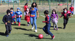 Desde el 5 de enero que la cancha del Campus San Andrés se llena de niños y niñas entre los 3 y los 13 años. Son cerca de 140 hijos e hijas de trabajadores de la UCSC, que de lunes a viernes, entre las 9 y las 13 horas, disfrutan de Verano Recreativo 2022 con juegos, música, baile y talleres de ciencias, cocina, teatro y expresión junto a un grupo de monitores, los que en su mayoría son alumnos de 2do año en adelante en las facultades de Medicina y Educación de la misma Universidad y con experiencia previa en el trabajo con menores. Carolina Baier, jefa de la Unidad de Bienestar y Formación de Personas, cuenta que este programa se lleva realizando hace 11 años y que comenzó como una actividad más recreativa durante el período de vacaciones y que con el tiempo se fueron sumando otros actores de la propia casa de estudios, convirtiéndose en “un programa más integral, no solo de recreación, sino de aprendizaje, deportivo, de vida saludable. Como Unidad y como Dirección, hemos crecido con esta actividad porque al principio participan 40 niños y ahora es con inscripción y desde diciembre nos preguntan cuándo comienza. Algunos que partieron de chiquititos, ya son apoyo de monitores o monitores fijos que enseñan a los nuevos integrantes.” Pese a la experiencia alcanzada en más de una década, realizar esta versión implicó un reto no menor. “Por la pandemia, el año pasado fue a través de modalidad sincrónica. Este año pensamos hacerlo dos veces a la semana, pero después las autoridades nos aprobaron todos los días”. Sobre los cuidados que han tenido, Carolina dice que se han regido por los protocolos Covid es decir uso de mascarilla, la cual se cambia varias veces por jornada, desinfección de manos con alcohol gel, colaciones individuales para los niños, sumado a otras acciones como la toma de PCR a los monitores una vez a la semana o informar de contactos estrechos para tomar rápidamente los exámenes, en resumen “harta preocupación y protección para los niños.” Respecto a este mismo tema, Constanza González, Coordinadora de Verano Recreativo 2022, agrega que otra medida ha sido la toma de temperatura a los niños antes que entren a la cancha. Para Constanza el objetivo de esta actividad es simple. “Que los chicos no estén en sus casas y que vengan acá a pasar un verano entretenido, con actividades recreativas y deportivas. En general son chicos, que por la pandemia, no han salido mucho y ahora han podido compartir, conocer otra gente, otros niños y están felices”. Cuenta también que este año Verano Recreativo se hizo en dos modalidades, una en Campus San Andrés y la otra en la sede Los Ángeles. “Es la primera vez que se lleva a cabo en esa sede, donde tuvimos la participación de 10 niños. Se realizó por tres días, nada más.” Verano Recreativo 2022 concluye este lunes 24 de enero, jornada que tiene contemplada varias sorpresas, como la instalación de camas saltarinas, el desarrollo de una kermés con palomitas y una variada agenda de actividades que harán sentir a los pequeños como en un circo.